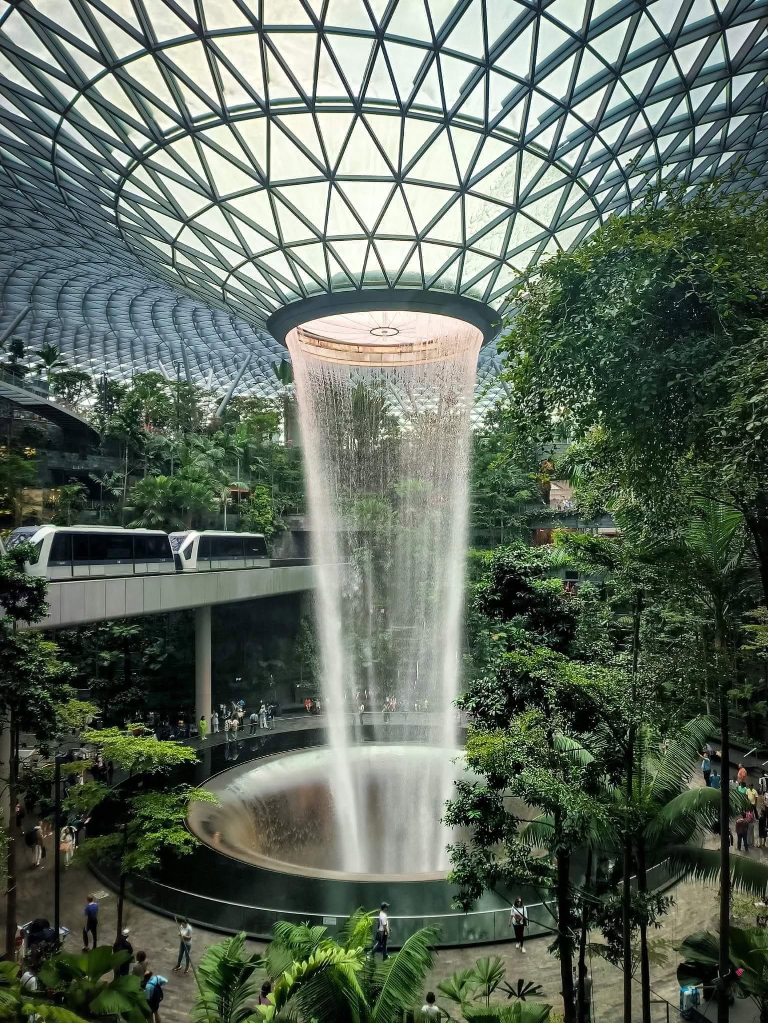 The HSBC Rain Vortex indoor waterfall inside the glass dome of Jewel Changi Airport surrounded by greenery