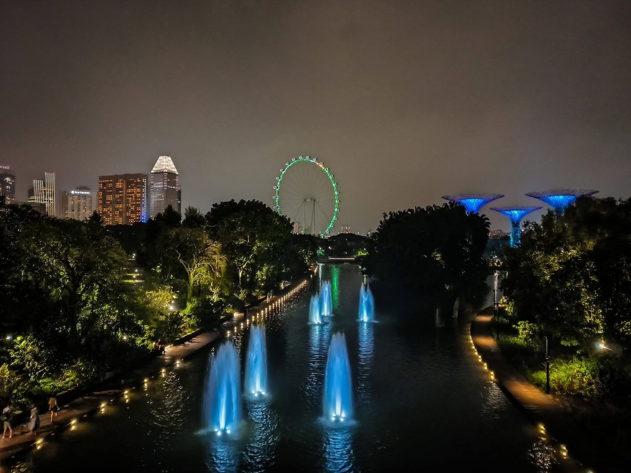 Night view of the fountains and walkway at Gardens by the Bay with the Singapore Flyer and Supertrees illuminated in the background